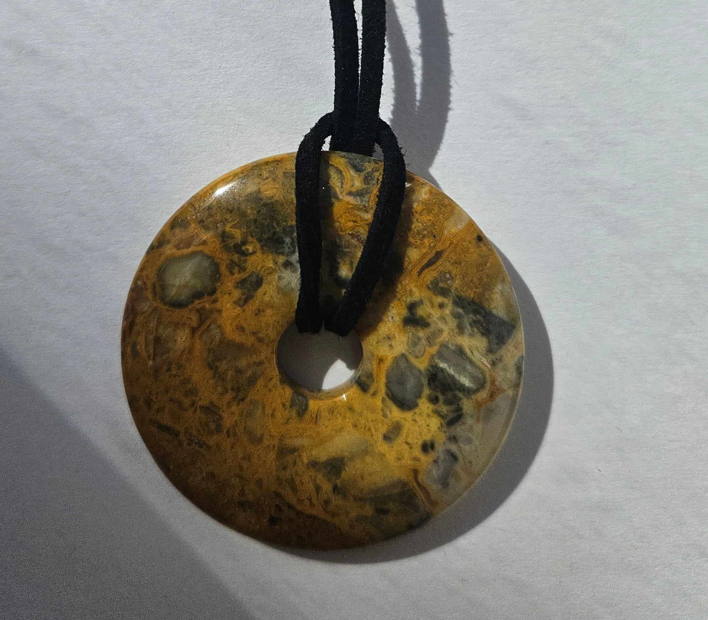 Round stone pendant on a black cord against a white background