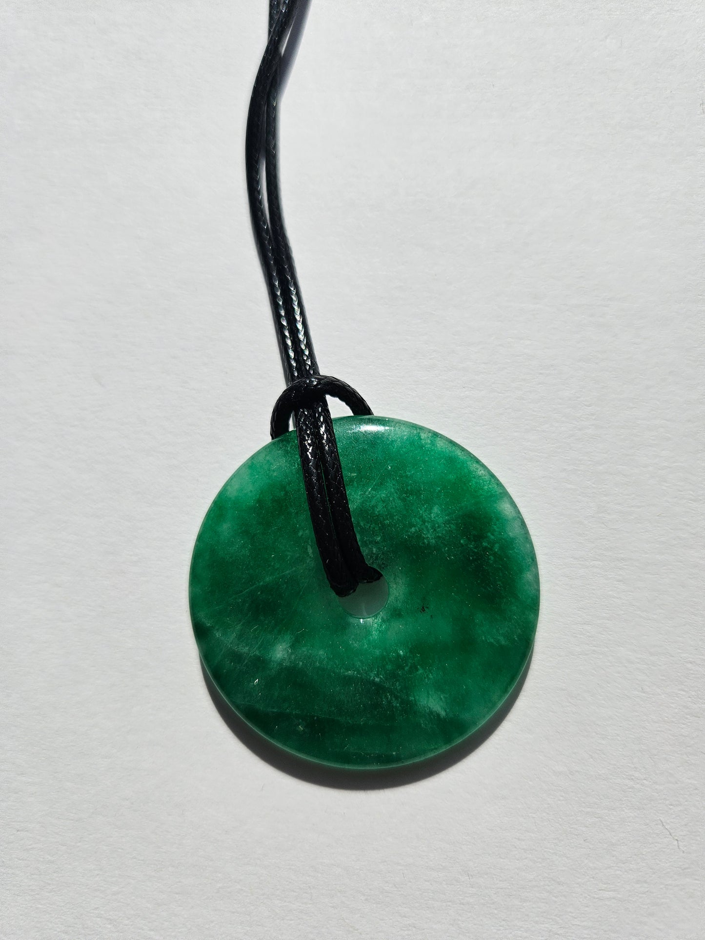 Green jade pendant on a black cord against a white background