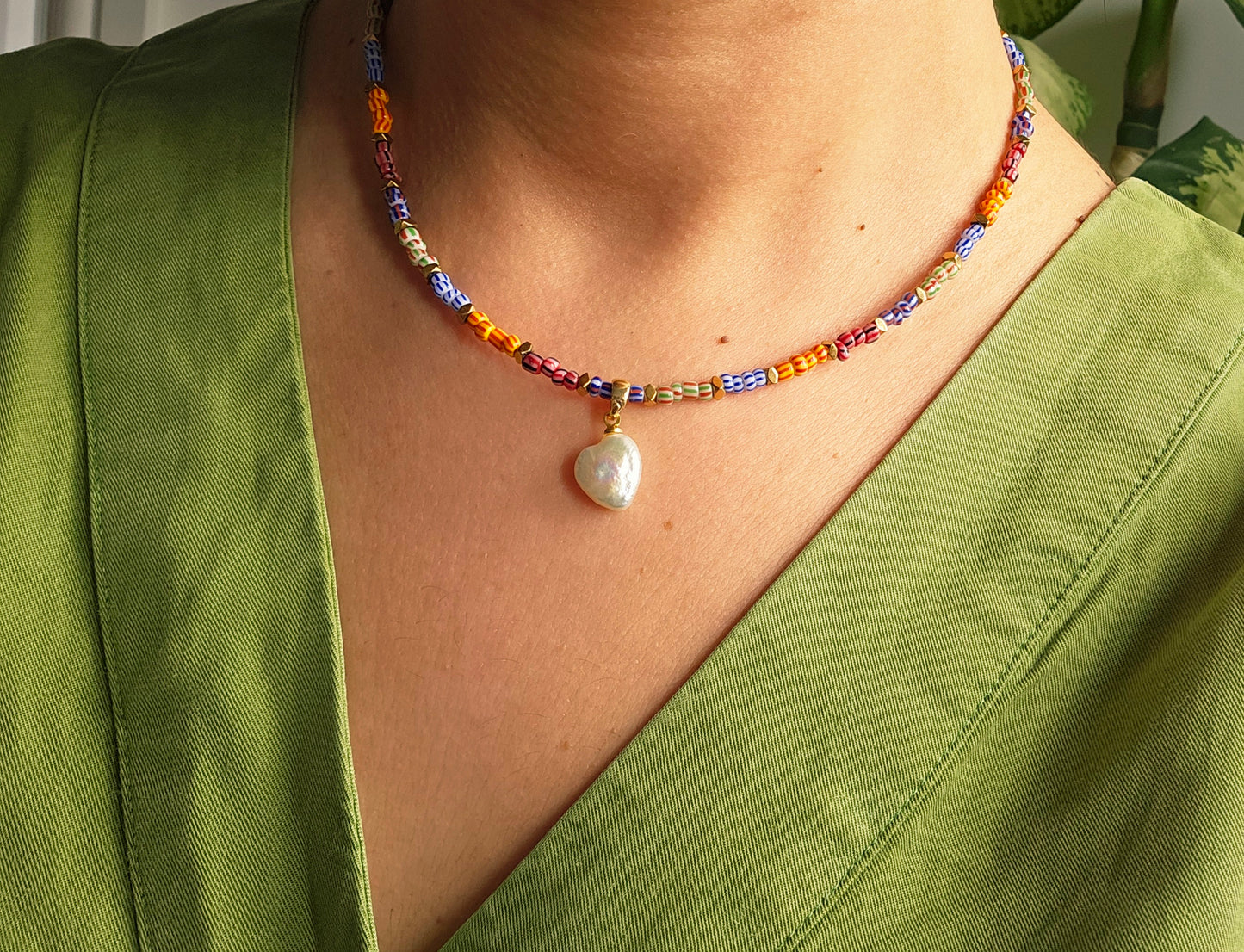 Colorful beaded necklace with a heart-shaped pendant worn by a person in a green outfit.