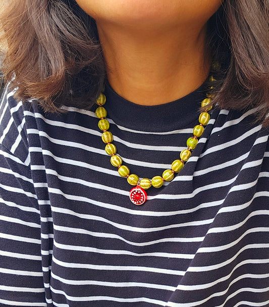 Person wearing a striped shirt and a yellow beaded necklace with a red pendant.