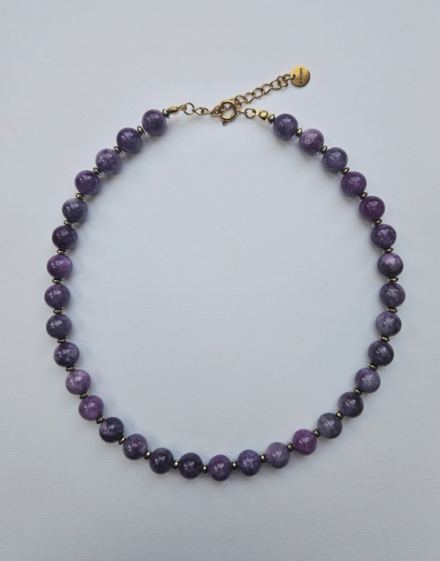 Purple beaded necklace with a gold clasp on a light gray background