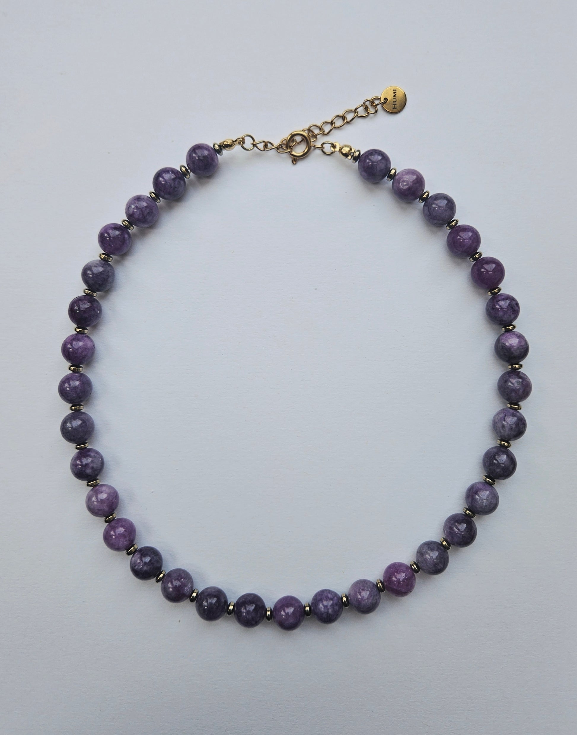 Purple beaded necklace with a gold clasp on a light gray background