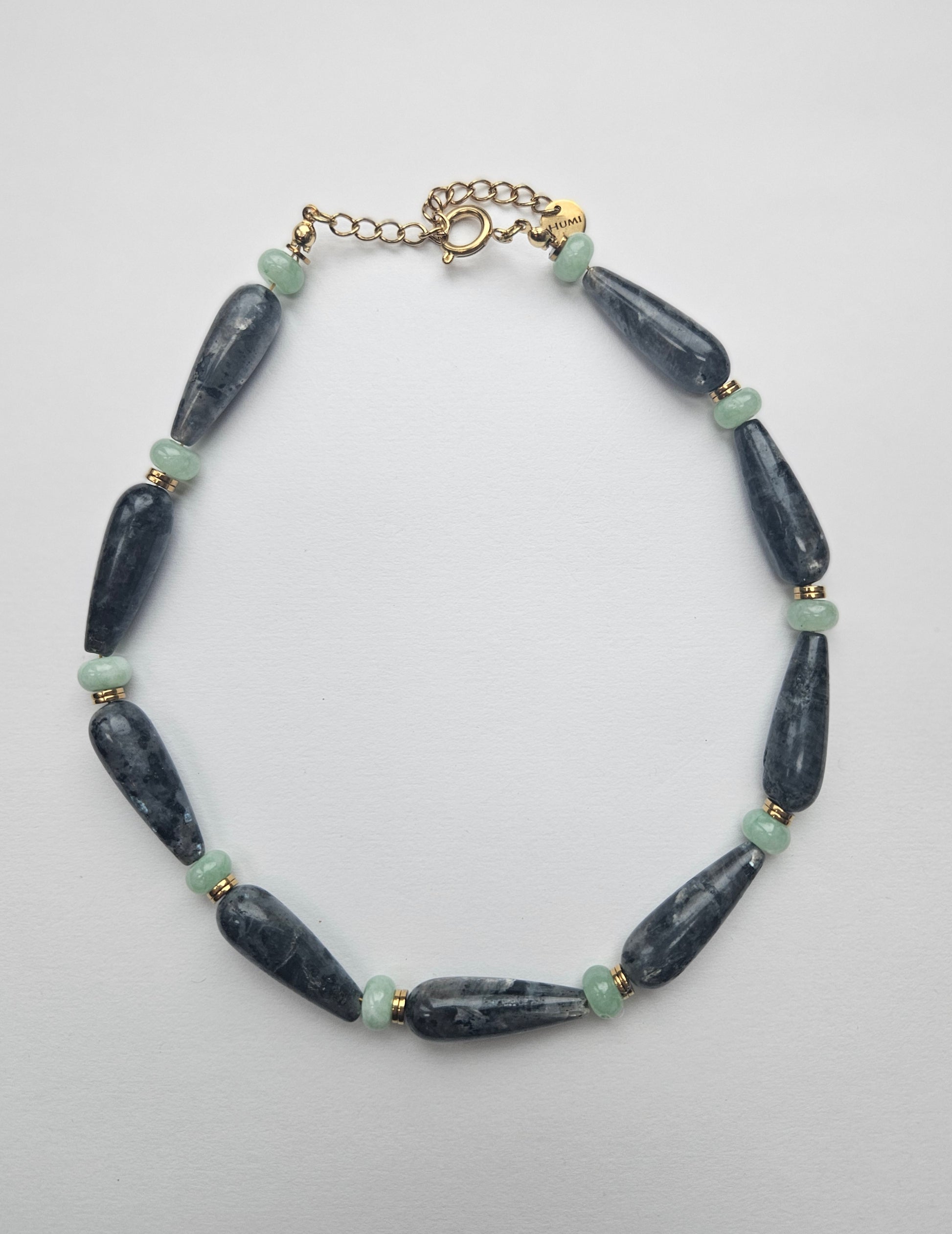 Necklace with dark grey and green beads on a light grey background