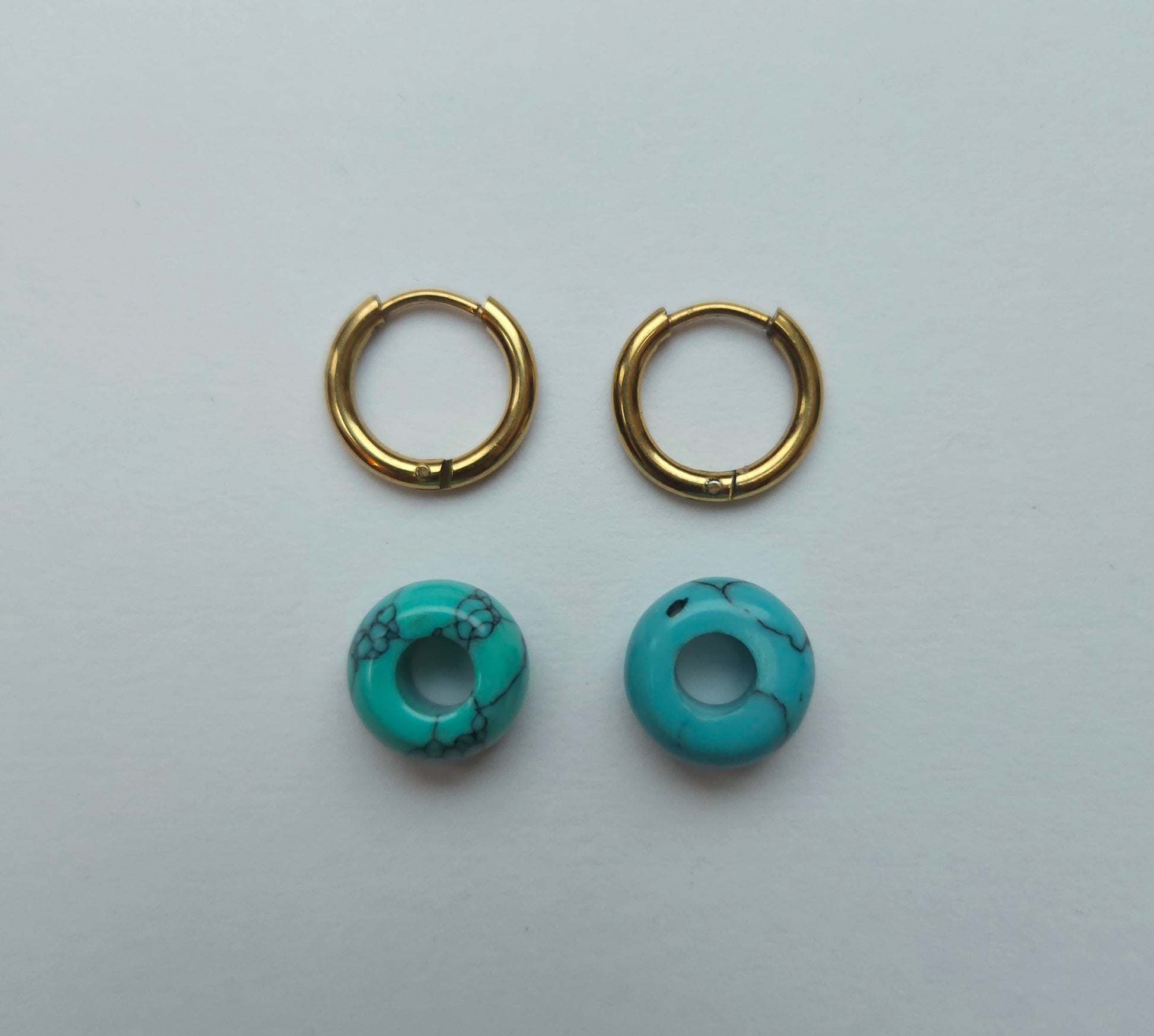 Gold hoop earrings with turquoise stone beads on a light gray background