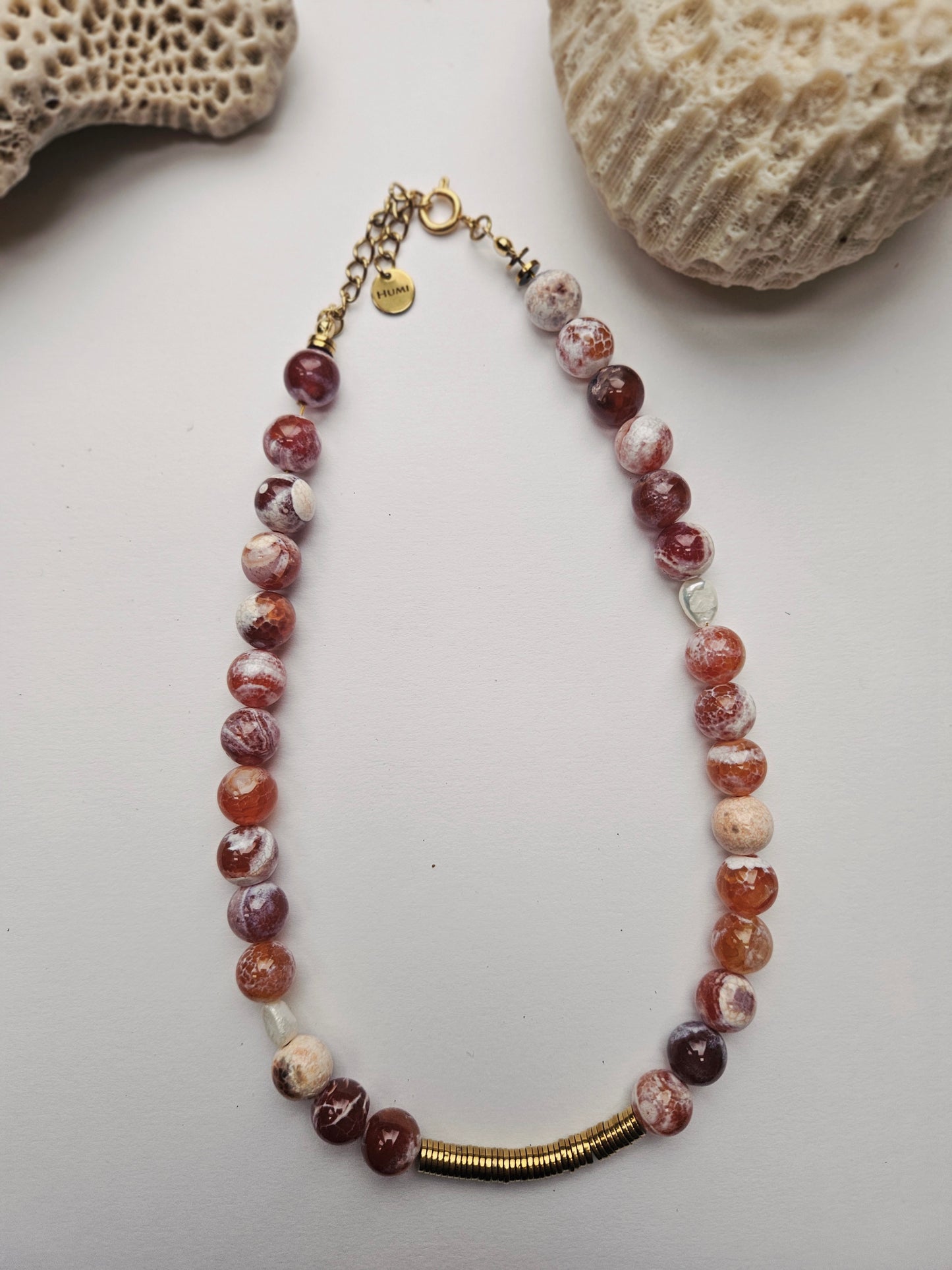 Necklace with multicolored beads and gold accents on a white surface with rocks in the background
