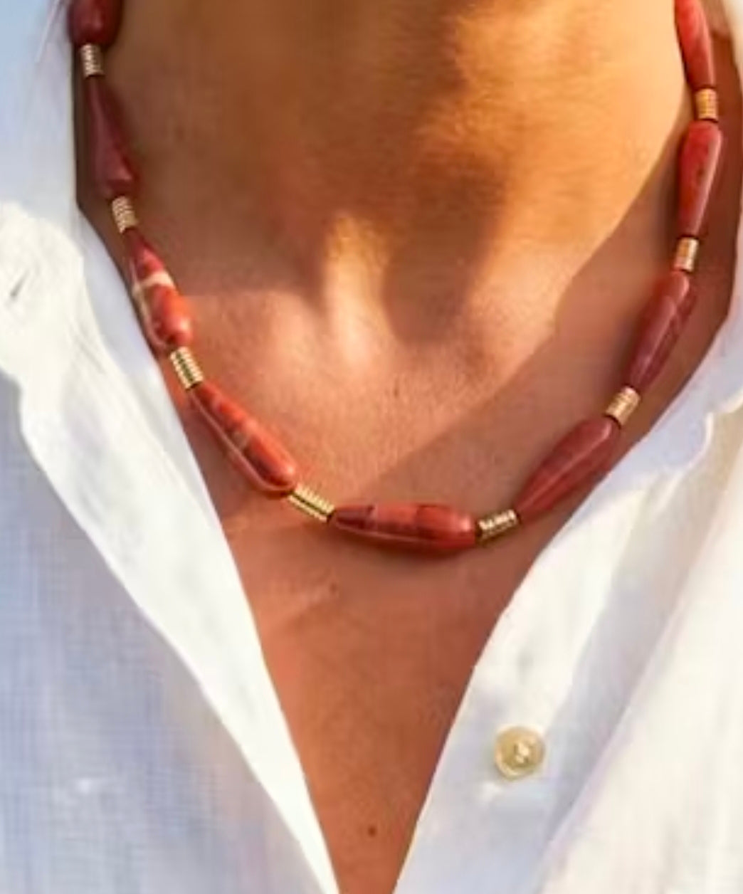 Red beaded necklace with gold accents worn by a person against a white shirt background