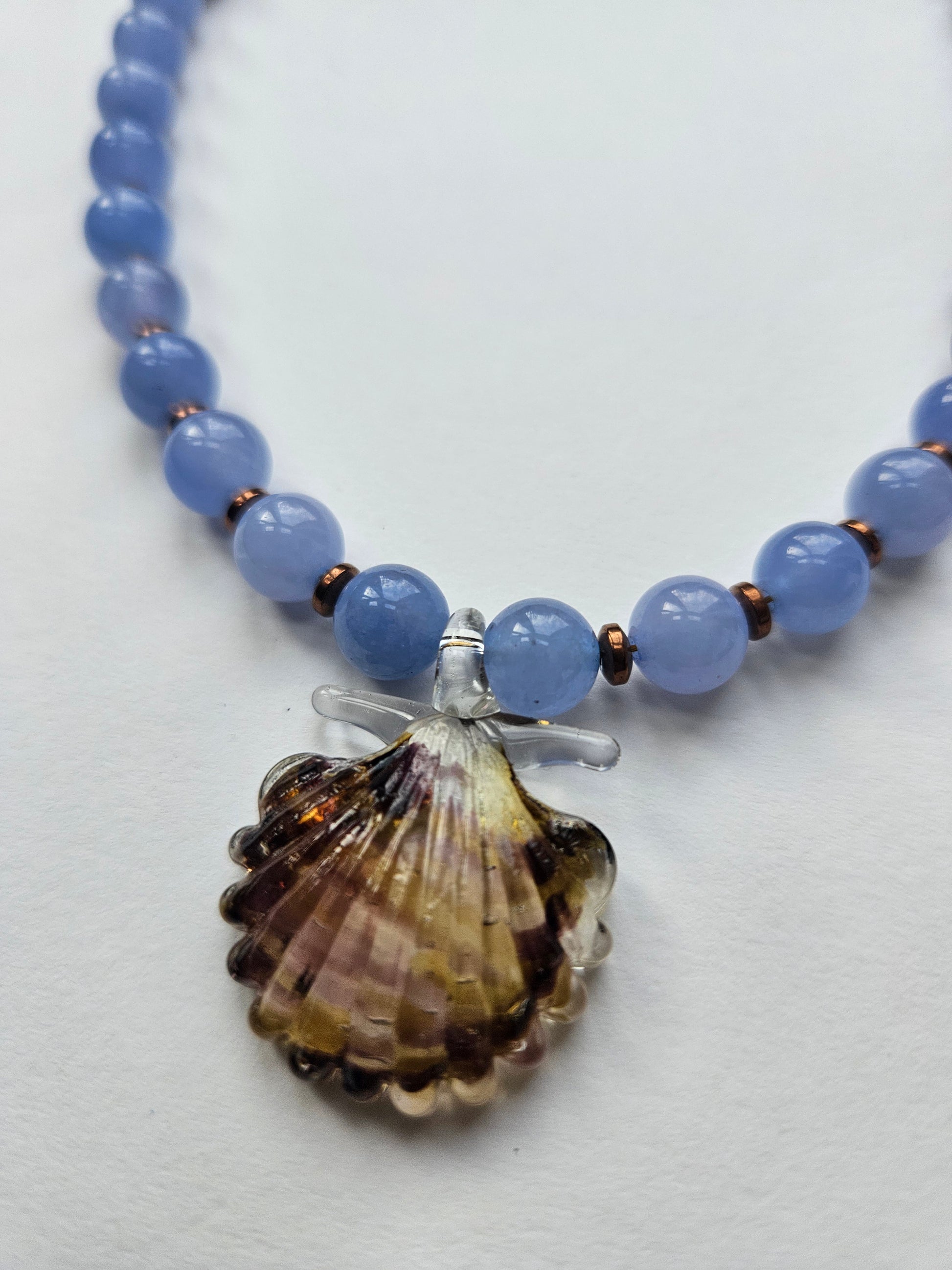 Blue beaded necklace with a shell pendant on a white background