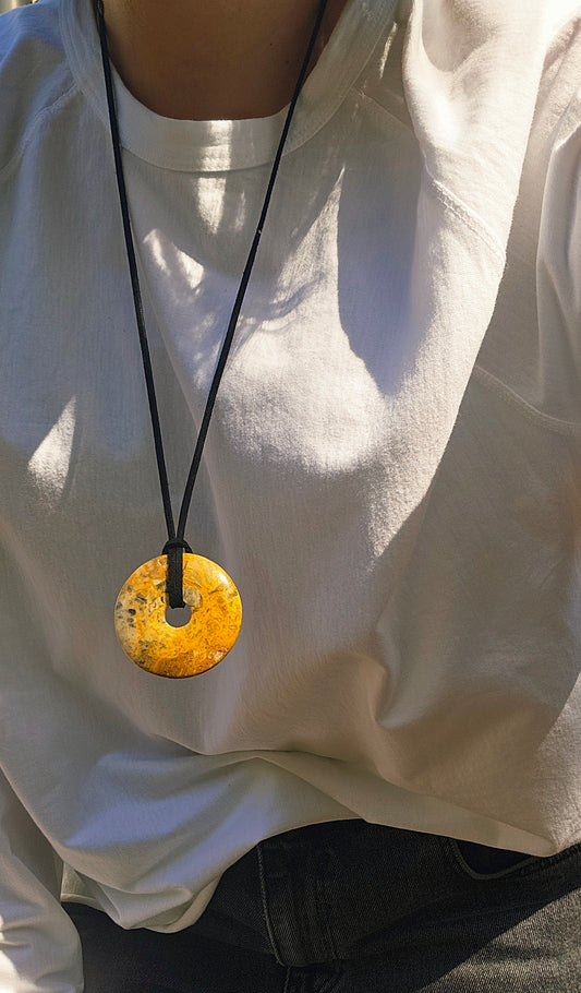 Person wearing a necklace with a large round pendant on a plain background