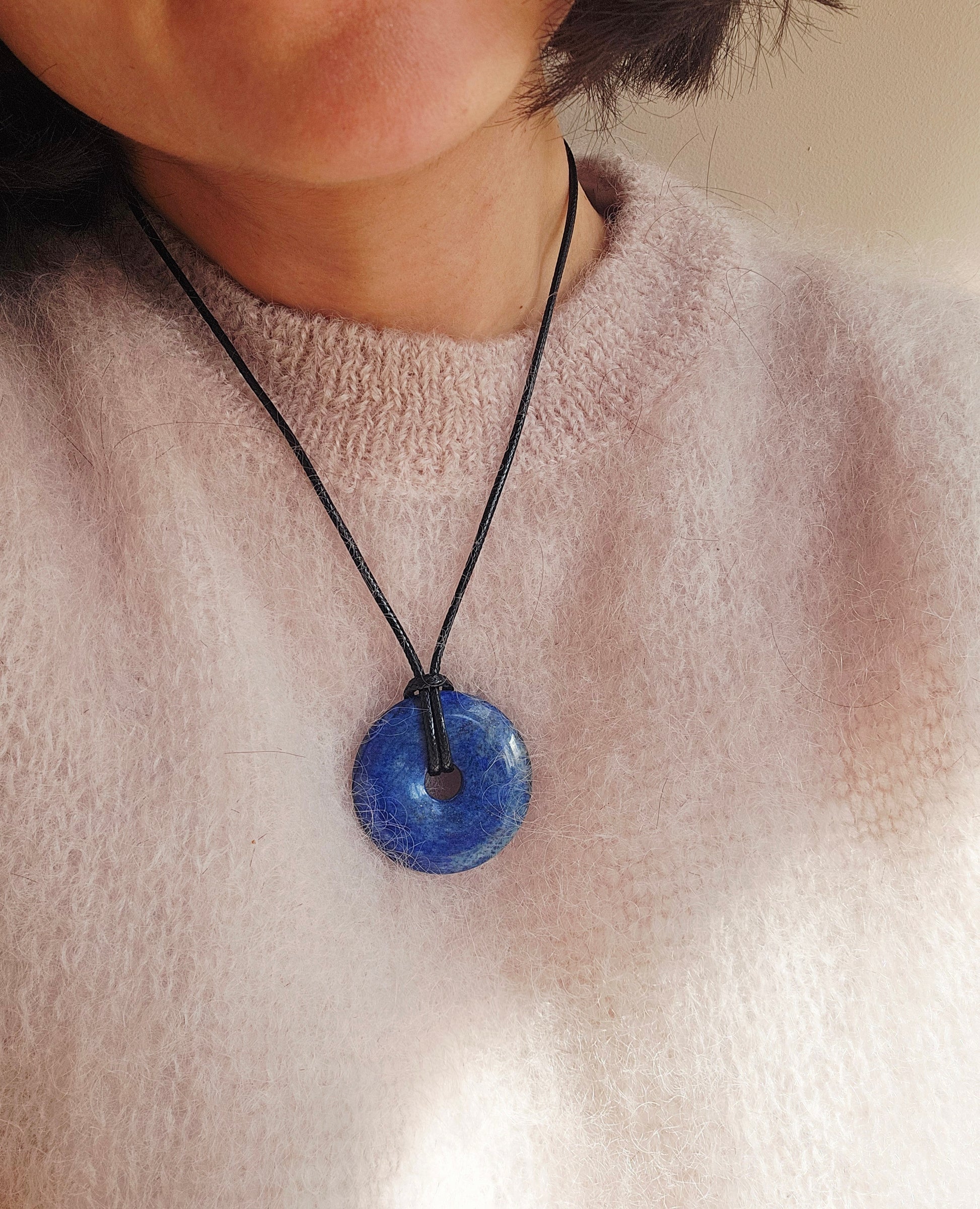 Person wearing a necklace with a blue pendant on a plain background