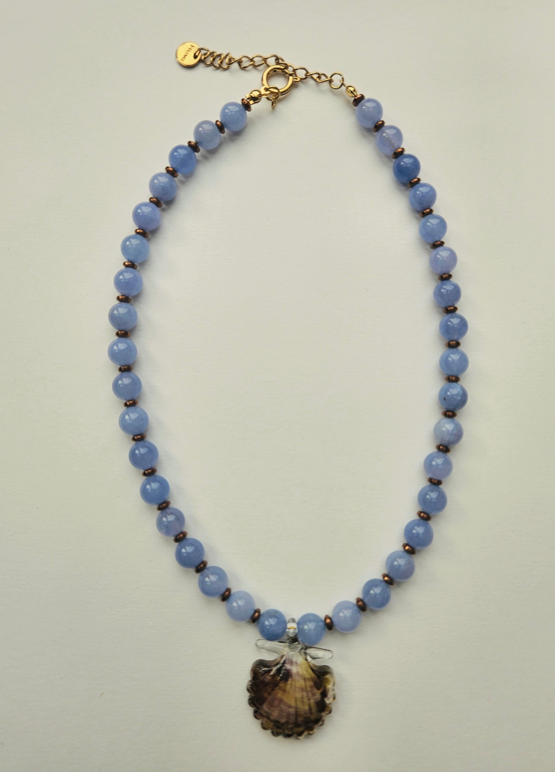 Necklace with aquamarine blue beads and a brown shell pendant on a light gray background
