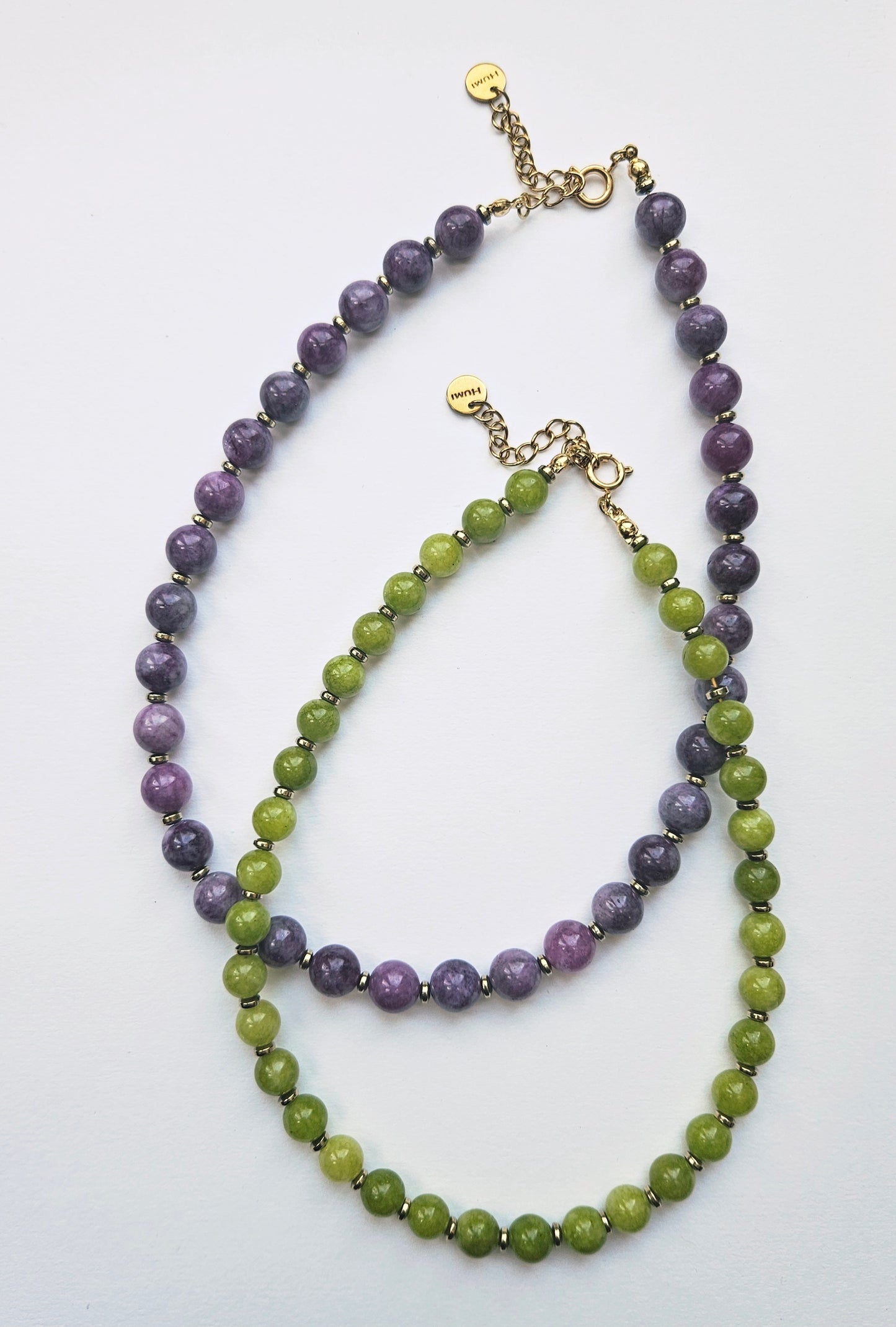Two beaded necklaces, one purple and one green, on a white background