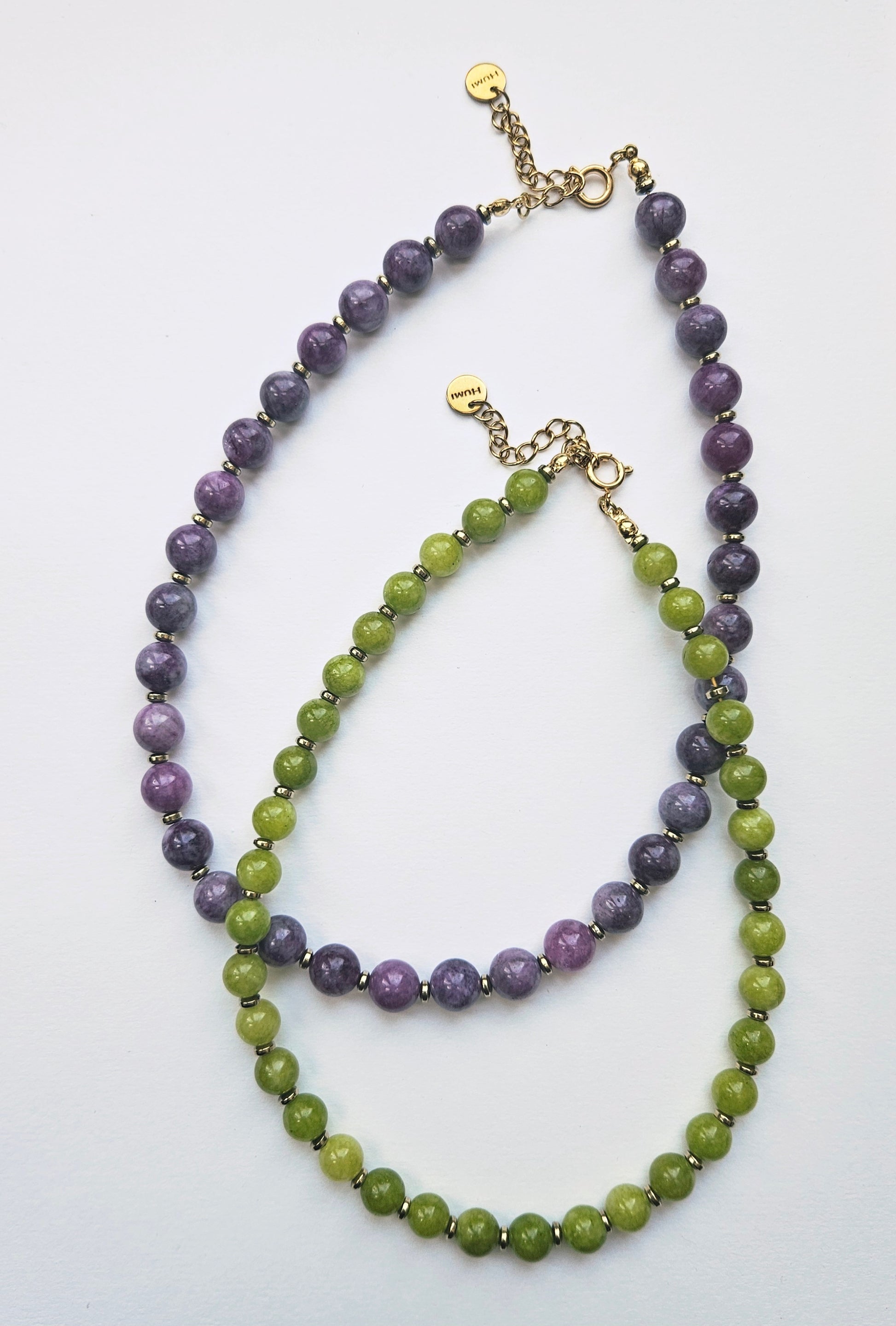 Two beaded necklaces, one purple and one green, on a white background